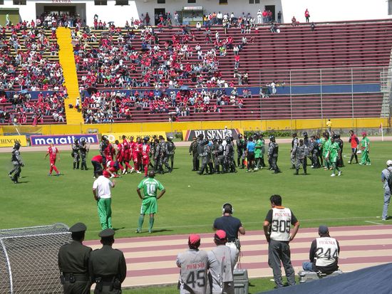 Hier spielen nicht Schwarz gegen Rot. Die schwarzen Typen sind Polizisten, die sich als "Freund und Helfer" nuetzlich machen! Und kein Wunder tragen sie Helme ...