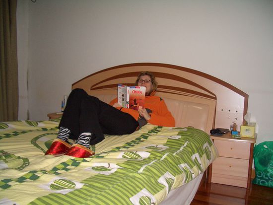 Sandra in Zebrasocken mit roten Kitschhausschlappen kulturell-interessiert auf ihrem Bett