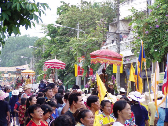 Unmengen von Buddhafiguren werden schuetzend unter Schirmen durch die Stadt gefahren....