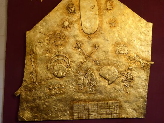 Goldplatte mit Symbolen der Inkazeit. In der Mitte das Stern des Südens. links davon die Erde mit Bergen und Regenbogen, rechts der Titicacasee. Oben Sonne und Mond. Unten Lagerhäuser, die den Reichtum symbolisieren sollen.