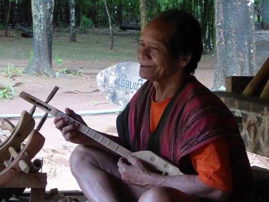 Der Mann spielt ein einfaches Saiteninstrument, wahrscheinlich eine Phin Phia