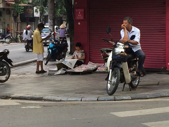 auf der anderen Strassenseite verkauft eine Frau Zeitungen