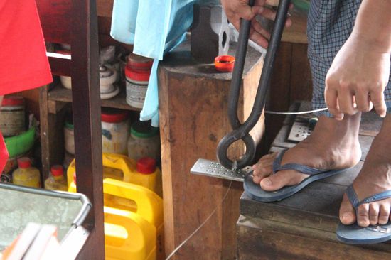 Der Silberdraht wird von Hand durch immer dünnere Ösen gezogen, damit ein ganz dünner Draht entsteht, aus dem man Kettenglieder herstellen kann.