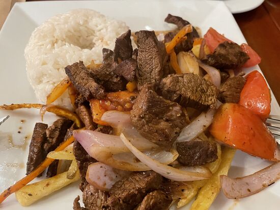 Lomo saltado, ein traditionlles Gericht aus Rindfleisch mit Tomaten und viel Zwiebeln, angerichtet auf Pommes, serviert mit Reis.