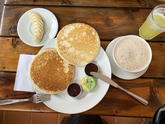 Pancakes mit Honig und Banane, dazu eine heisse Schokolade und ein Ananassaft