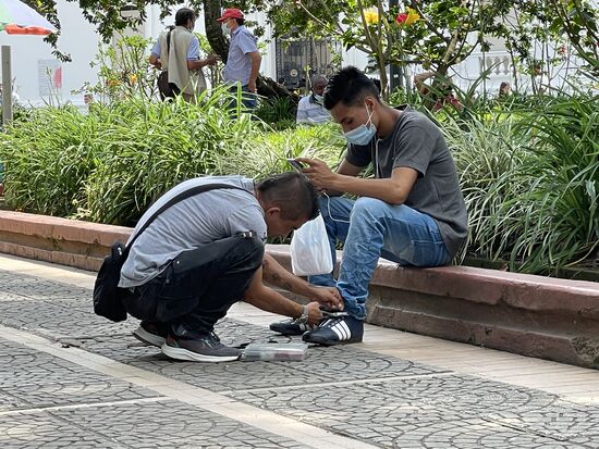 Der Schuhmacher wechselt die Farbe der Ösen ambulant, während sein Kunde sich ein Video streamt.