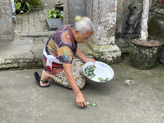 Eine ältere Frau legt ihre Opfergaben auf die Strasse vor ihrem Hauseingang