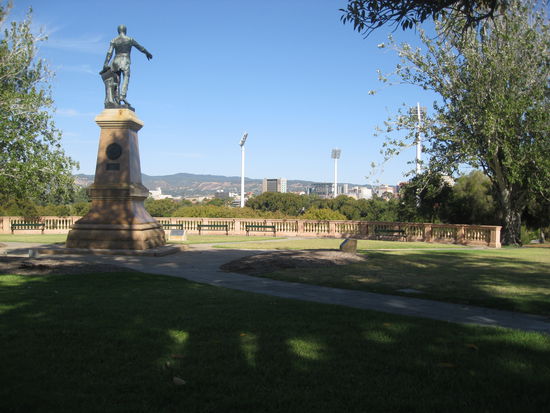 Statue vom Stadtplaner von Adeleide, die Flutlichtmasten im Hintergrund gehoeren zum Adeleide Oval (Footballstadion)