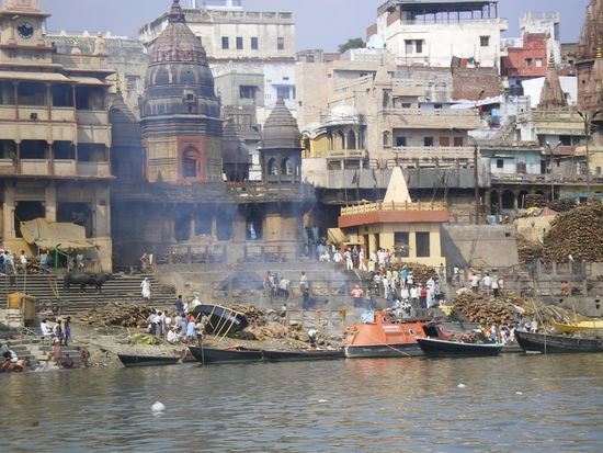 eines der verbrennungsghats. vom boot aus darf man u.u. fotographieren. links im bild das hospiz, ringsum brennholz. asche und reste werden in den ganges geworfen, ein paar meter weiter baden die menschen. aber man sagt, die schwermetalle aus firmen oberhalb von varanasi, die ins wasser geleitet werden, sind viel fuer die menschen schlimmer als ausscheidungen und reste von verstorbenen im fluss