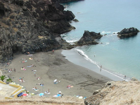 Eine Badebucht mit feinem schwarzen Sand und einer Strandbar.