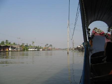 Am Klog mit dem Longtailboot unterwegs. Links und rechts die auf Pfählen gebauten Häuser und der Strommast steht auch im Fluß.