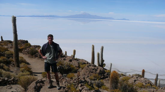 Auf dem Salzsee liegt eine hauchduenne Wasserschicht. Hinterm Vulkan am Horizont wartet Chile.