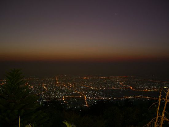 Und von der Aussichtsterasse in die andere Richtung: Chiang Mai in beginnender Morgendaemmerung (ca. um 6:00, Sonnenaufgang ist etwa um 6:50). Schoen zu sehen: das Quadrat der Old City, wo sich die Touristen aufhalten (sowas wie der 1. Bezirk in Wien) - mit den beiden hellen Strassen, die hinein- bzw. hinausfuehren.
