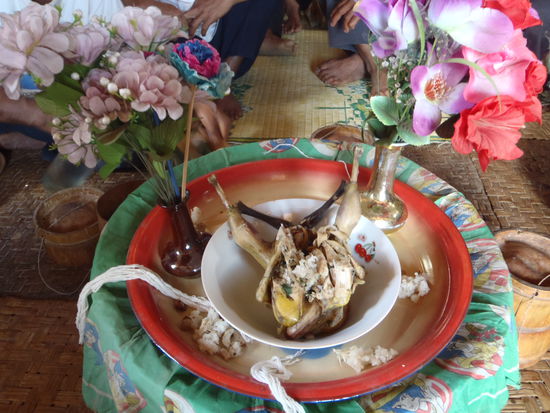 Zeremonie fuer den Willkommensgruss. Das Huhn wird gleich zerteilt und mit Suppe gegessen. Der Reis ist in den Bambusbehaeltern auf dem Boden (Seite). Die Baendchen bekomme ich umgebunden.