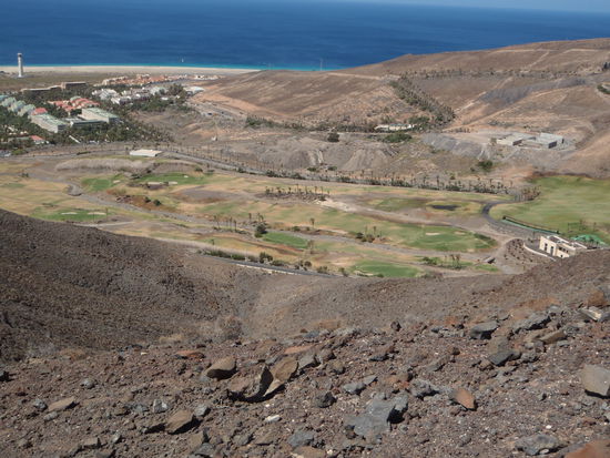 Blick zurück auf den Strand mit Leuchtturm von Morro Jable und ein Golfplatz - ohne Spieler und ziemlich ausgetrocknet.