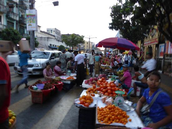 Obst-Highway in Yangon
Der beste Platz für den Obststand ist mitten auf der Straße, dort kaufen die Autos im Vorbeifahren ihre Tüten ein. es bildet sich in der Mitte eine zweite Gasse für Fußgänger, der Bürgersteig selbst ist noch rechts, außerhalb. Dazu musst Du wissen, dass die Autos keine Rücksicht nehmen wie in Thailand, hier springst Du als Fußgänger auf die Seite (hab ich bei den Einheimischen abgeguckt!).