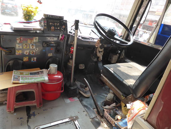 ﻿Das Bus-Cockpit: Schalt-Knüppel bis zur Schulter, ein Schuh für das grobe, weil gefahren wird in flip Flops. Unterm Sitz die Kappe von dem Energie-drink, der verleiht Flügel. Der Lappen um das Lenkrad saugt sicher Überschüsse von Schmieröl auf. Ein weiterer Lappen wird nass gemacht (Wasser ist im roten Eimer) und die Spiegel geputzt sowie die mit Tape stabilisierte Ablage und dient dann für die Kleingeld Ablage während der Fahrt. Auf den kleinen Schemeln darf der bus boy solange sitzen, bis notplaetze gebraucht werden.