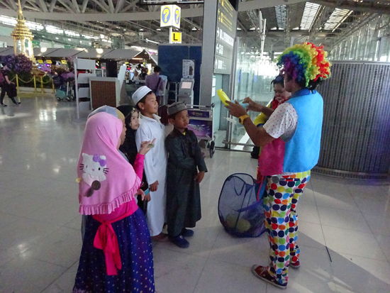 Ein Clown beschäftigt Kinder aus Malaysia am Bangkok Suvarnabhumi International Airport