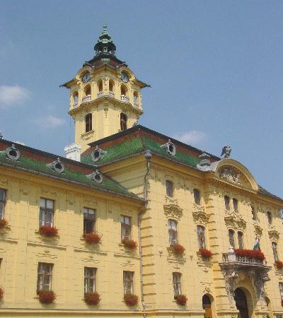 Szeged 2003 - das Rathaus (Teilansicht). Das Glockenspiel im Turm erklingt jede Viertelstunde.
Neben dem Rathaus erhebt sich ein noch vor dem Hochwasser erbautes Gebäude, das Bérhàz, in dem sich die Amtsräume des Bürgermeisters befinden. Es ist mit dem Rathaus über die sogenannte Seufzerbrücke verbunden - gemäss dem Vorbild der bekannten Brücke in Venedig.
(Ironie: Wie mancher Bürgermeister bewegt sich hin und wieder auf einer virtuellen Seufzerbrücke?)