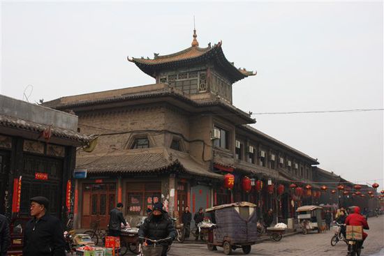 Hier fährt in der Bildmitte gerade ein deckenbehängtes Tuk Tuk um die Kurve.