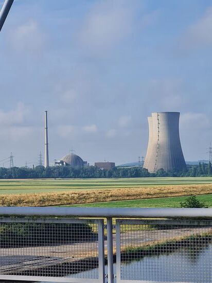 In der Vergrößerung sieht man den hinteren Turm etwas nach links gewandt herausstehen.
Von links gesehen der schlanke Abluftkamin des Reaktorgebäudes, das kuppelförmige Reaktorgebäude selbst, das dunkelgraue, rechteckige Maschinenhaus mit einer Hochdruck- und zwei Niederdruckturbinen, sowie dem Generator.
Zuletzt die nicht mehr bestehenden Kühltürme.