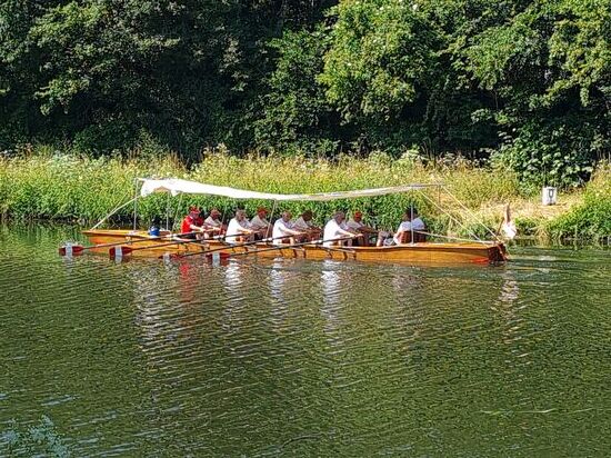 Eine gemütliche Rudergemeinschaft in Form eines Achters mit zwei Steuermännern in nicht-olympischer Sitzanordnung zieht gemächlich seine Bahn flußabwärts bei Volkach.