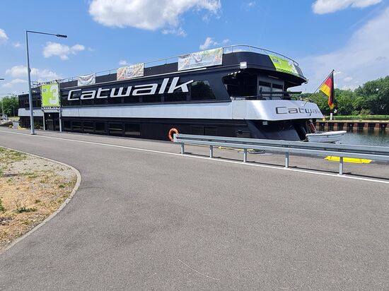 Die "Catwalk", das Bayern 3 - Partyschiff für max. 700 Passagiere, 45,8 m lang, 9,3 m breit, 0,8 m Tiefgang und 2 x 300 PS Maschinenleistung pausiert an der 
Neuen Mainlände in Kitzingen.
Die Catwalk fährt jährlich die schiffbaren Flüsse Bayerns ab und bietet den Passagieren genügend Möglichkeiten zum Abfeiern bis zum geht nicht mehr.