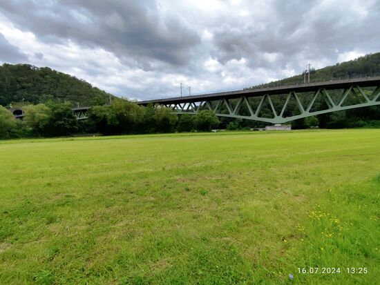 Es handelt sich dabei um das Portal des Schönraintunnels, der direkt in die Maintalbrücke Nantenbach übergeht. Im Tunnel verläuft die sog. Nantenbacher Kurve, eine Ausfädelung der Bahnstrecke von Würzburg nach Frankfurt aus der Neubaustrecke von Würzburg nach Fulda. Im Tunnel und über die Brücke kann bis kurz vor der Einfädelung in die Altstrecke aus Gemünden in Richtung Frankfurt am Main mit bis zu 200 km/h geeilt werden.
Ein paar Daten zur ästhetisch recht gut geglückten Nantenbacher Maintalbrücke
(ausgezeichnet mit dem Stahlinnovationspreis 1994):
Die gewölbte (gevoutete) "Stahlfachwerkverbundbrücke" (Strombrücke über den Main) ist gut 374 m lang, bei einer größten Stützweite von 208 m.
Die direkt anschließende Vorlandbrücke ist eine 6-gliedrige Stahlbetonbrücke mit insgesamt 317 m Stützweite.