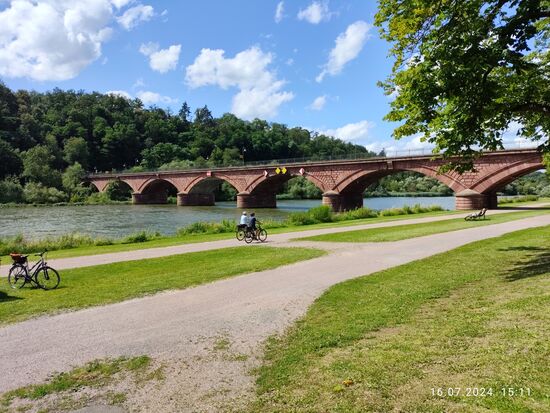 Südansicht mit Sonnenlichtbeflutung.
Für eine Verbreiterung der Durchfahrt wäre eine Entfernung des mittleren Brückenpfeilers nötig. Die Silhouette im Stadtwappen und der bestehende Denkmalschutz stünden jedoch laut Stadt dagegen. Laut Netz gab es Anfang 2021 noch keine Entscheidung, wobei ein neues Gutachten des Staatlichen Bauamts vom September 2024 diese Forderung vom Tisch bringen.
Ich habe den betreffenden Zeitungsartikel über das Gutachten nicht über die Anfangszeilen hinweg freischalten lassen, somit denke ich, daß die Statik dann nicht ausreichen dürfte. Weiterhin sind die Mainschleusen auch nicht breiter als ein Bogen.
Allerdings wäre die Gefahr eines Rammens bei einem Steuerfehler auf dem Schiff bei einer größeren Durchfahrtsweite geringer.