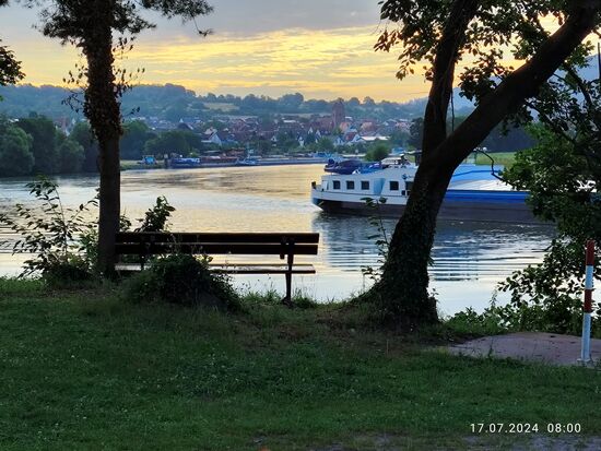 Rückblick auf Dorfprozelten bei morgendlicher Stimmung an der ersten Mainwindung.
Ein nicht identifizierter Binnenfrachter befindet sich auch bereits auf seiner weiteren Tour. Diese Schiffe legen abends an geeigneten Plätzen an bzw. gehen vor Anker. Nachts ist also Ruhe. Bei Containertransporten oder Festterminen dagegen wird in der Regel "durchgefahren", wobei dann meist ein zusätzlicher Steuermann an Bord ist.