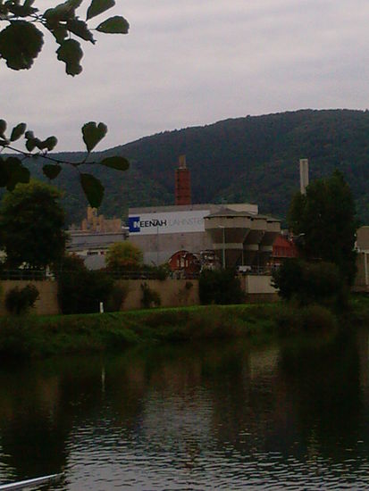 Papierfabrik Neenah Lahnstein.
Das ocker-gelbliche Bauwerk im Hintergrund, das links vom Firmenlogo zu sehen ist, stellt Schloss Stolzenfels auf der anderen (linksrheinischen) Seite des sich nahenden Rheins dar.