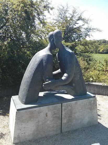 Am nördlichen Beginn der Donaubrücke eine Skulptur mit Bezug auf den Gedenkstein bei Lutzingen wenige km vorher: (Aus einer Internet-Info) 
"Wir befinden uns hier bei Kilometer 2530,4 der schönen Donau südlich von Höchstädt. An eine der entscheidenden Schlachten im spanischen Erbfolgekrieg zwischen den kaiserlich-englischen Truppen und dem französisch-bayerischen Heer "erinnert" hier die von Ernst Steinacker erschaffene Skulptur: "Wenn Feinde sich umarmen".
"Am schönen nahegelegenen Donauufer kann man sich gut Gedanken über die Statue und ihre Inschrift (Vorderseite) machen. Für Fahrradfahrer ein Drive-In, Autofahrer sollten besser den angegebenen Parkplatz verwenden."
Für mich war's wirklich ein Drive-In, da ich mir meine Marschverpflegung vom Frühstück in Form der üblichen üppig belegten Wurst-Käse-Semmel als aufgeschobenes Mittagessen gegen 14:15 Uhr verinnerlichte.
Weißwürste hätten ja auch trotz der späten Zeit gut angestanden, am besten gleich südlich der Donau, aber wie diese erhitzen...