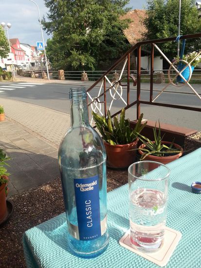 Nach einem anstrengenden Tag ein Odenwald-Wässerchen als Durstlöscher auf der Speise-Terrasse des Gasthauses. Auf der anderen Seite der Straße fließt hinter dem Geländer das Flüsschen Mümling.