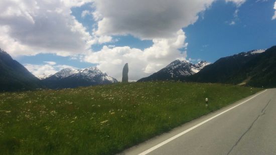 Zwischen den Bergen im Hintergrund ein übermannsgroßes Steindenkmal in vielleicht 100 m Entfernung, das etwas abgesetzt von der Bergstraße stand.