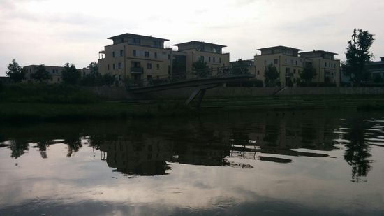 Vom westlichen Ufer ragt (leider etwas schlecht erkennbar) auf Höhe des linken Wohngebäudes eine Aussichtsplattform über die Wasseroberfläche.