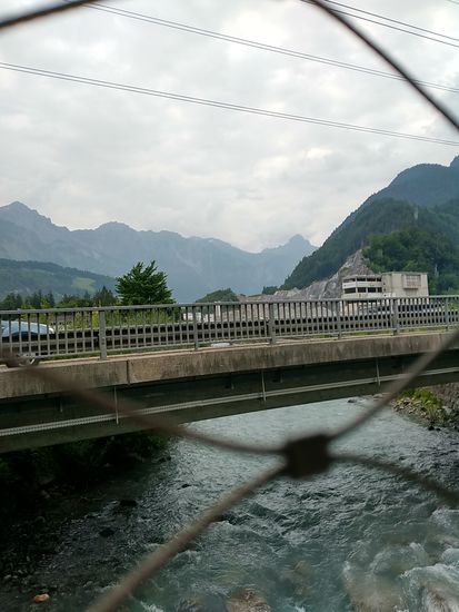Kurz hinter der Stadt Bludenz bei Lorüns, dem in meinem Fall Schlußort des Walgau-Radwegs, überquere ich auf der Alfenzbrücke den gleichnamigen 26 km langen Hauptfluß des Klostertales, das im Bildhintergrund vor der Bergkette nach rechts verläuft. Dort verläuft auch die Arlberg-Schnellstraße, sowie die Arlberg-Eisenbahnstrecke über St. Anton am Arlberg in Richtung Landeck / Tirol. Im kombinierten Arlberg-Eisenbahn und Straßentunnel verläuft die Grenze von Vorarlberg und Tirol, für manche Bewohner dies und jenseits so etwas wie eine Staatsgrenze, wenn man den Erzählungen Glauben schenken will. Ich registriere sowas für einen "Schmäh" und konzentriere mich als Rad-Fernreise-Tourist weiterhin auf die landschaftlichen Aspekte dieser überaus beeindruckenden Tour. 
Die Alfenz fließt ja aus Richtung Bildhintergrund unter mir durch, um kurz hinter mir in die Ill zu münden, die von rechterhand aus dem Montafon, einem 39 km langen Tal, das von der Bielerhöhe (meinem Tour-Hauptziel) bis Bludenz reicht und von der Ill durchflossen wird, die ich ja schon seit ihrer Mündung in den Alpenrhein gegen ihren Lauf per Rad erkunde.
Für mich als (Ober-)Bayern ist auch sehr interessant, daß das Montafon ("Muntafu") von 1805 bis 1814 zum Königreich Bayern gehörte, dann wieder zu Österreich. 
Da hat ja seinerzeit die große Politik ganz schön hin- und hergeschoben...
