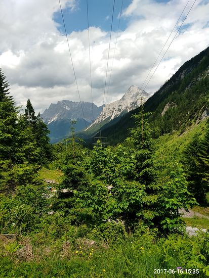 Der erste Blick auf das in dunkel erscheinende Zugspitzmassiv. Der rechts viel näher gelegene und deshalb höher erscheinende helle Berg könnte die Sonnenspitze (2416 m) sein, ist aber von der Bedeutung her gegenüber dem Zugspitzmassiv nur nebensächlich.
