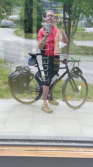 Pseudo-Selfie an einer großen, spiegelnden Glasscheibe des Pegelgebäudes von Landeck am Fluß Sanna.