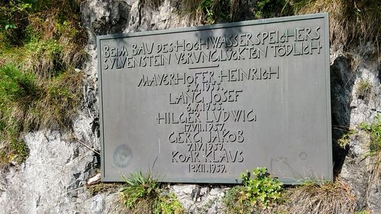 Eine Gedenktafel für die fünf beim Bau des Sylvensteinsstausees tödlich verunglückten Arbeiter.
Hier steht zwar Hochwasserspeicher, was sich bei den Hochwassern 1999 und 2005 sehr bewährte, grundsätzlich sollte der Speicher mit 7 km Länge, 2 km Breite und 124 Mio. m³ Stauraum aber für einen konstanteren Wasserspiegel der Isar sorgen.