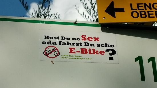 Auf der vergrößerten Hinweistafel für Bad Tölz haftet ein humoriger Aufkleber, der sich gegen E-MTBs wendet.  
Ich muß aber allgemein, nicht nur bzgl. E-MTBs erwähnen, daß ich entgegen mehrerer vorangegangener Ferntouren im ganzen Verlauf der Isartour erstaunlich wenige E-Bikes gesehen habe. Also eine Tour der Altmodischen...