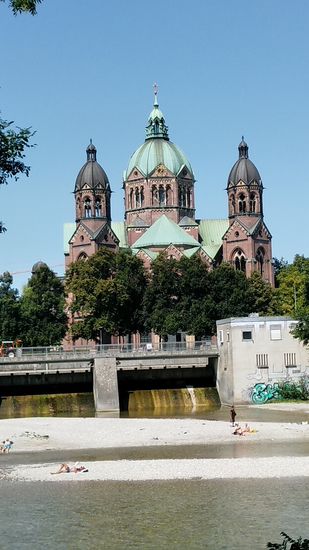 Auf der gegenüberliegenden Westseite der Isar erscheint auf etwa halbem Weg zwischen dem Deutschen Museum und dem Maximilianeum die protestantische Kirche St. Lukas aus den 1890er-Jahren mit romanischer und neugotischer Architektur.