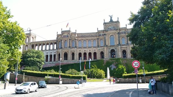 Über dem Ostende der Maximiliansbrücke, auf die ich kurz hochgefahren bin, thront das 1874 endgültig fertiggestellte, mit der stadtseitigen 150 m langen Schaufassade recht eindrucksvolle Maximilianeum, seit 1949 der Sitz des Bayerischen Landtags und bereits seit 1876 die Stiftung Maximilianeum für begabte Studenten aus der Pfalz und Bayern beherbergend.
Anschließend folgen noch drei Fotos als Vergrößerung und vom rechten Flügel, den ich bedingt durch den Baumbewuchs davor und der von einem näheren Standpunkt aus fehlenden Weitwinkel-Optik der Handykamera nicht als Gesamtobjekt ablichten konnte.