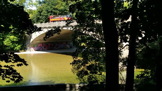 Wieder am Radweg zurückgekehrt, der kurz darauf unter der Äußeren Maximiliansbrücke hindurchführt, sieht man einen der zwei gleichlangen Brückenbögen (beide Bögen überspannen eine Länge von 96 m) aus Muschelkalkstein-Quadern, die die Fahrbahn aus Stahlbeton tragen.
Auf der Brücke befindet sich gerade ein oben offener Doppeldeckerbus, der sich mit Touristen auf City-Sightseeingfahrt befindet - ich selbst bin ja auch auf
"Munich-Isar-City-Bike-Sightseeing-Tour" 