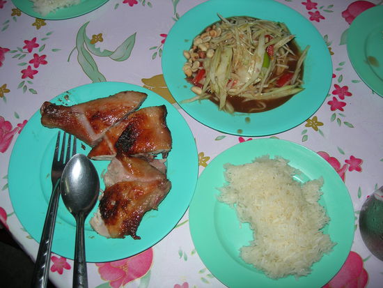 Papayasalat besteht u.a. aus: geraspelter gruener Papaya, Erdnuessen, Tomaten, Koriander, Ingwer, Kohl, Limettensaft und natuerlich Chilis.
Dazu leckeres frisch gegrilltes Haehnchen und Klebreis.
Das alles fuer 80 Baht (1.60 Euro)