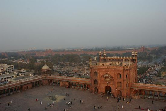 Blick auf das imposante Eingangportal mit einem Teil des Innenhofes der Jama Masjid. Im Hintergrund sind die Mauern des Red Forts zu sehen.