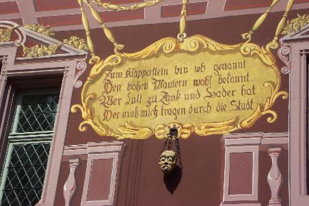 Der Klapperstein am goldenen Haus in Mulhouse. Wie die Innschrift sagt, mussten ihn die bösen Mäuler zur Strafe rittlings auf einem Esel reitend durch die Stadt tragen. Ein netter Brauch, leider wurde er abgeschafft