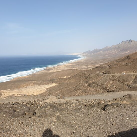 Blick in Richtung Cofete
Der Strand von Cofete ist kein Strand zum Baden. Er hat etwas mysteriöses an sich. Menschenleer, einsam, verlassen, im Hintergrund liegen die bis zu 800 m hohen Berge von Jandia an denen die Wolken hängen bleiben. Es weht immer eine starke Brise, die Wellen sind sehr hoch. Der Strand wirkt atemberaubend unheimlich, und doch wunderschön! Hier sollte man wegen der hohen Wellen und der starken Strömung nicht baden. Am ca. 2-3 km langen Strand liegen keine Touristen oder Einheimische, der Strand ist auch für Kinder absolut ungeeignet. Wenn man Fuerteventura besucht, sollte man sich mal einen Tag Zeit nehmen und diese unberührte Natur begutachten. Hier gibt es sonst nichts anderes zu sehen, außer evtl. noch die geheimnisumwogene "Villa Winter". Außerdem gibt auch noch das kleine Dörfchen "Cofete" mit einem Lokal.
