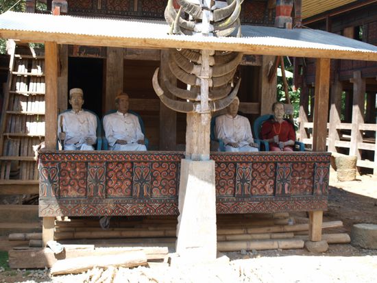 Diese Tau-Taus warten seit zwei Jahren gemeinsam mit den dazugehoerigen Leichen auf die tatsaechliche Beerdigung. Sie sind die letzten Gaeste ihrer Beerdigung, die bis aufs Begraben erledigt ist. Sie wollen nicht eher unter die Erde bzw. in den Fels, bevor nicht Hahnenkaempfe zu ihren Ehren stattgefunden haben. Die Sondergenehmigung der Regierung fehlt noch. Der Dorfchef meinte, dass das auch noch ein paar Jahre dauern kann. Damit die drei Jungs bis dahin nicht so allein sind, hat man das Tau-Tau ihrer vor 23 Jahren gestorbenen Mutter vom Grab dazugeholt.