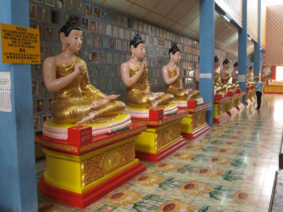 Dutzende dieser Buddhas sind im Tempel verteilt. An jedem kann der geneigte Glaeubige fuer einen anderen Zweck beten. 
Im Hintergrund sind verstorbene Gemeindemitglieder in Urnen beigesetzt.