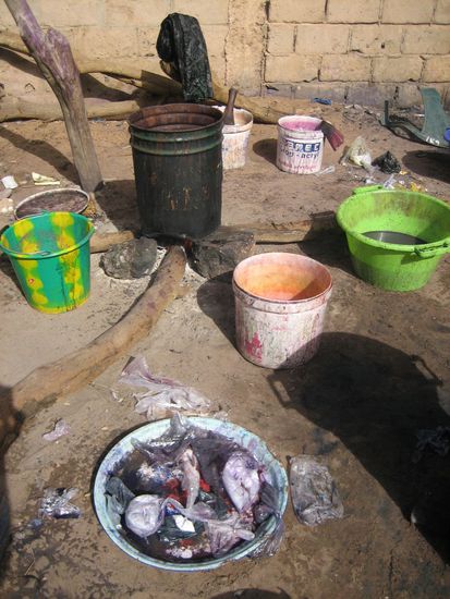 Vorne auf dem Teller liegen die Tütchen mit Farben und Fixierer, nebendran liegen leere Tütchen. Hinten sieht man die Feuerstelle die zum erhitzen des Färbewassers benötigt wird.